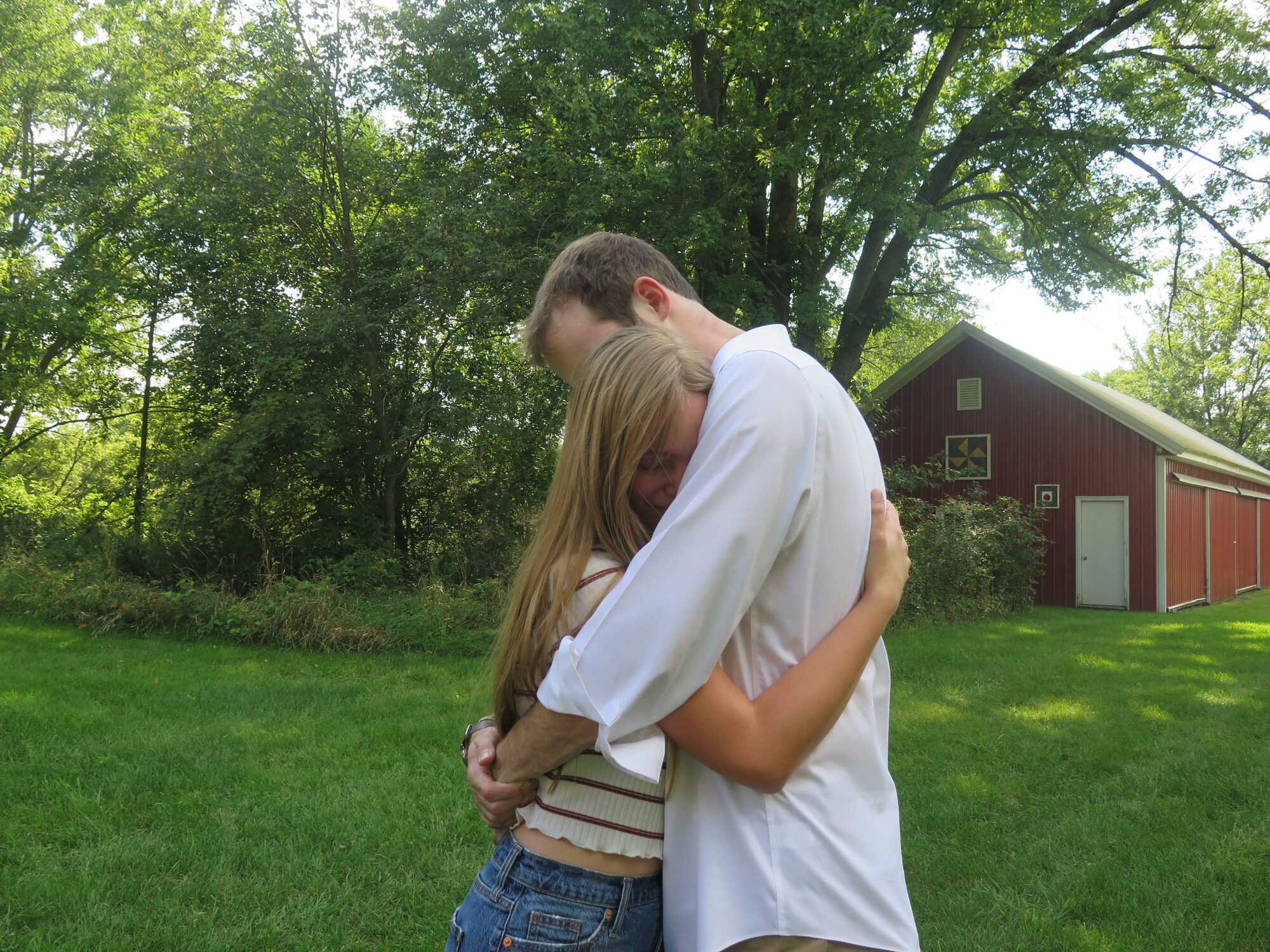Morgan and Samuel embracing on the lawn in front of a red barn